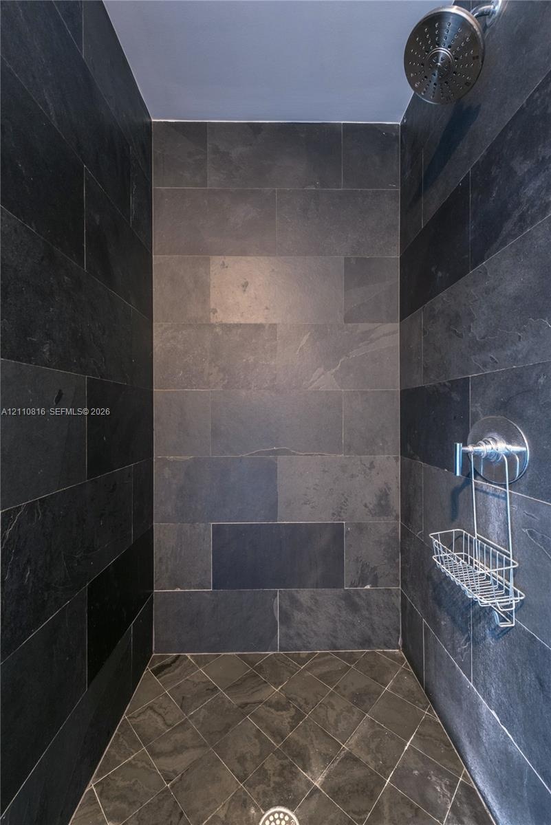 Walk-in shower enclosure featuring full-height charcoal stone tile walls, coordinating diamond-patterned tile flooring, a circular chrome showerhead, 