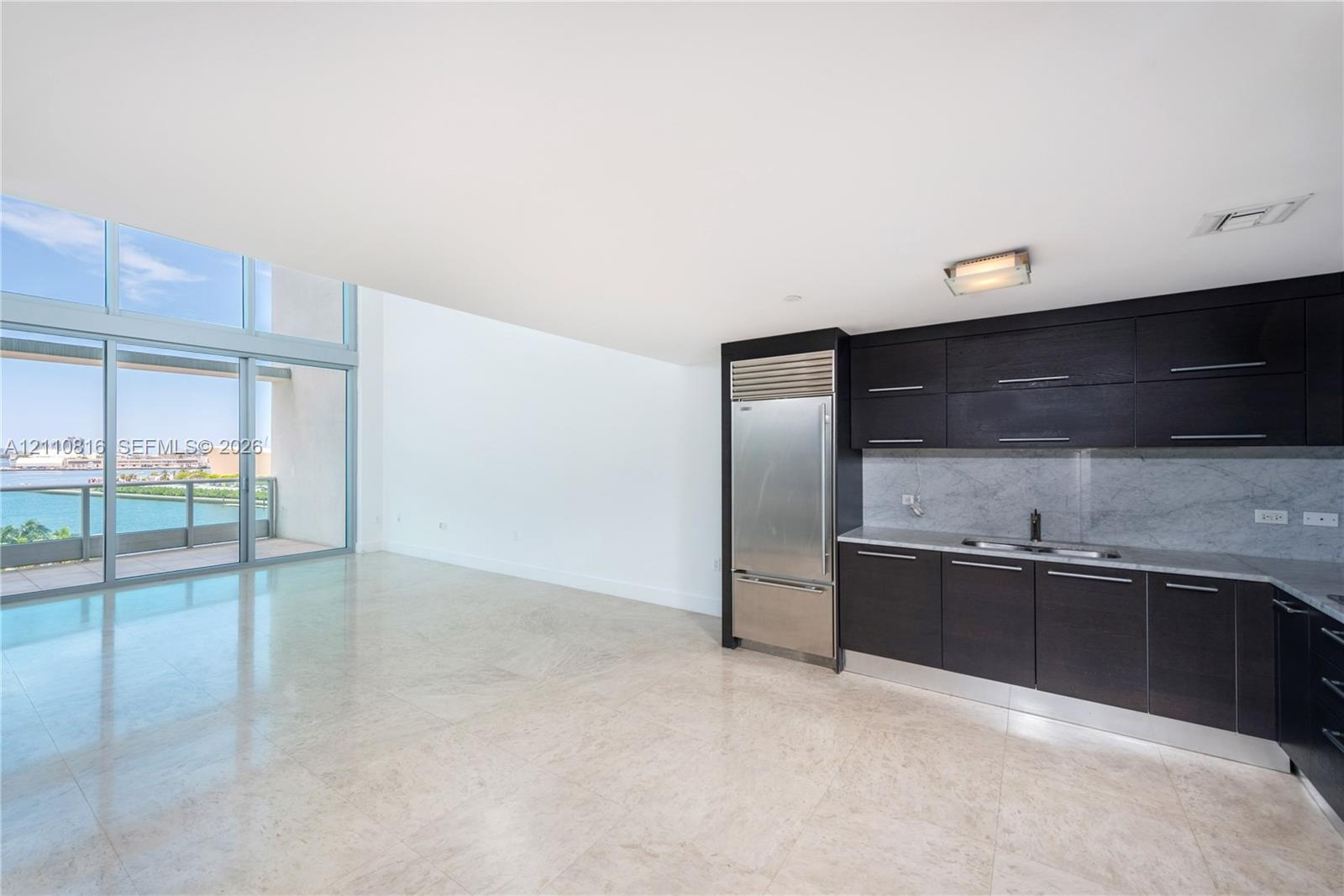 Kitchen featuring dark cabinetry, integrated stainless steel refrigerator, stone-style backsplash, and light-toned flooring, with floor-to-ceiling win