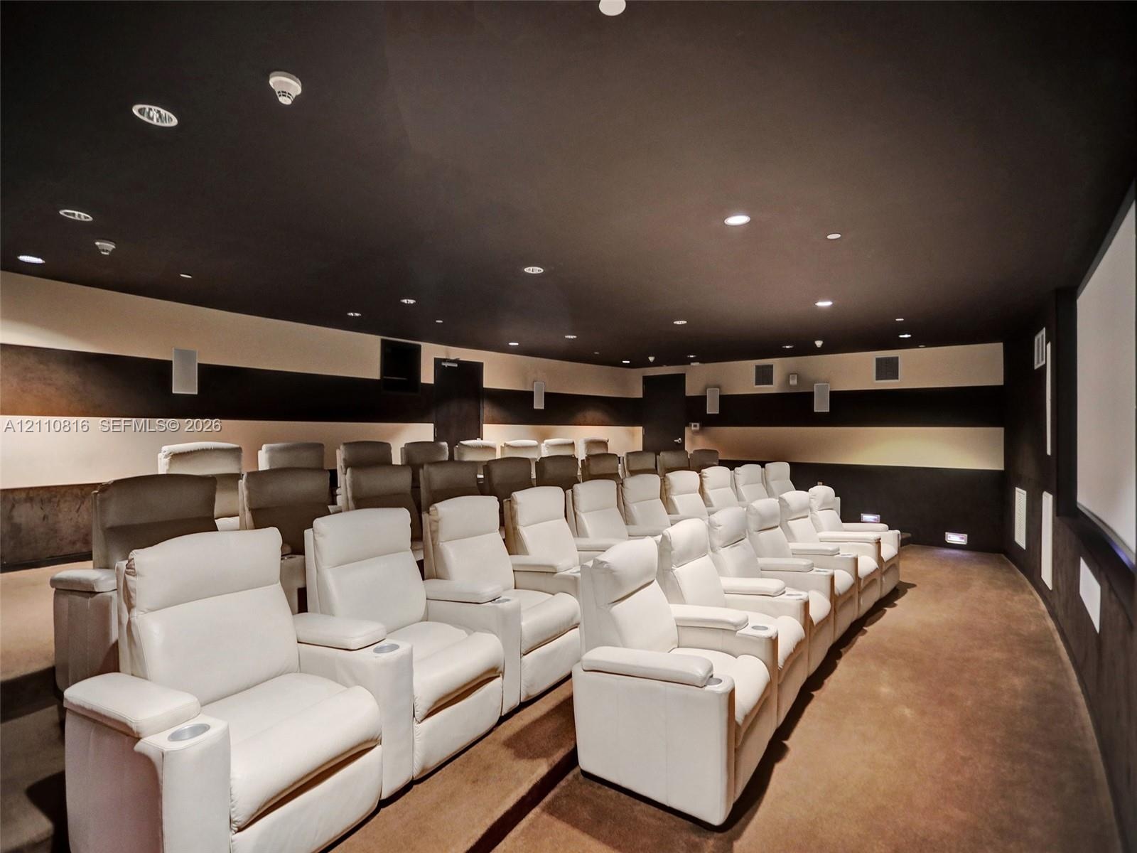 Dedicated media room featuring tiered platform flooring, integrated ceiling recessed lighting, wall-mounted speakers, and large-format projection scre