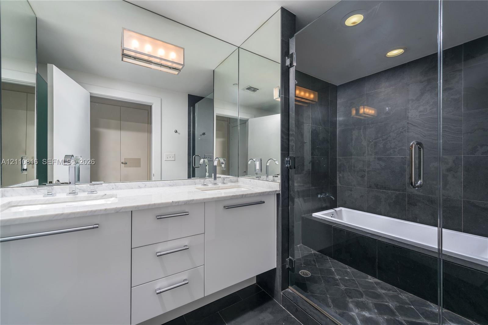 Bathroom featuring white cabinetry, stone-finish vanity countertop, dual undermount sinks with polished chrome fixtures, full-height vanity mirror, an