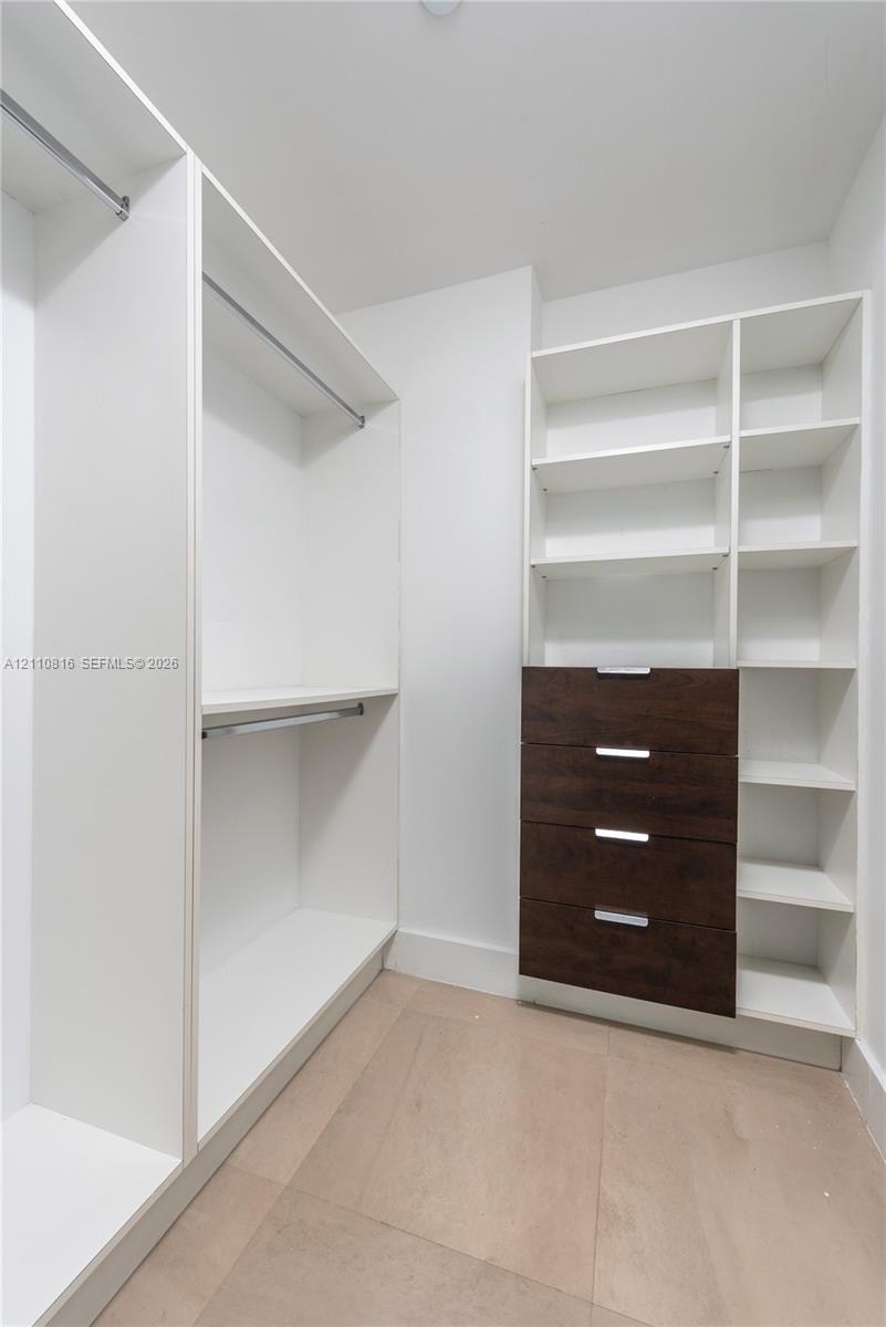 Walk-in closet featuring white built-in shelving, integrated hanging rods, a four-drawer dresser unit with dark-finish fronts, and light-toned floorin