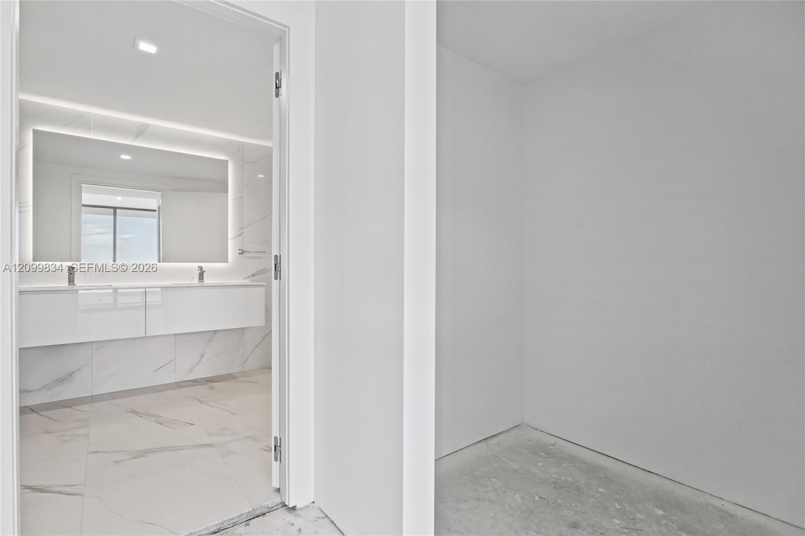 Bathroom featuring a wall-mounted double vanity, large-format tile flooring with veining detail, matching tiled wall surfaces, and a backlit vanity mi