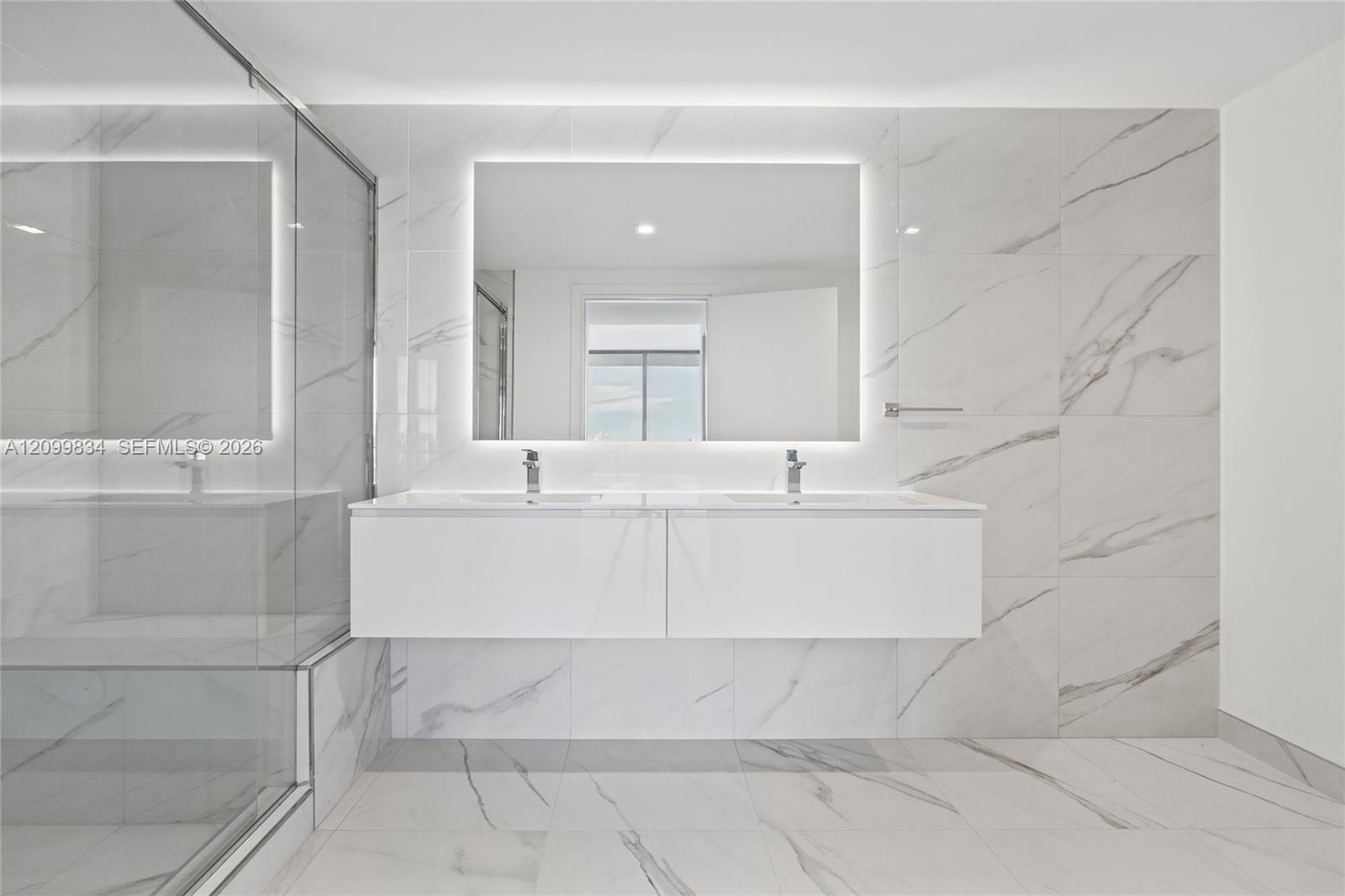 Double floating vanity with white cabinetry, rectangular vessel sinks, wall-to-wall rectified tile surfacing, backlit mirror, and glass-enclosed showe