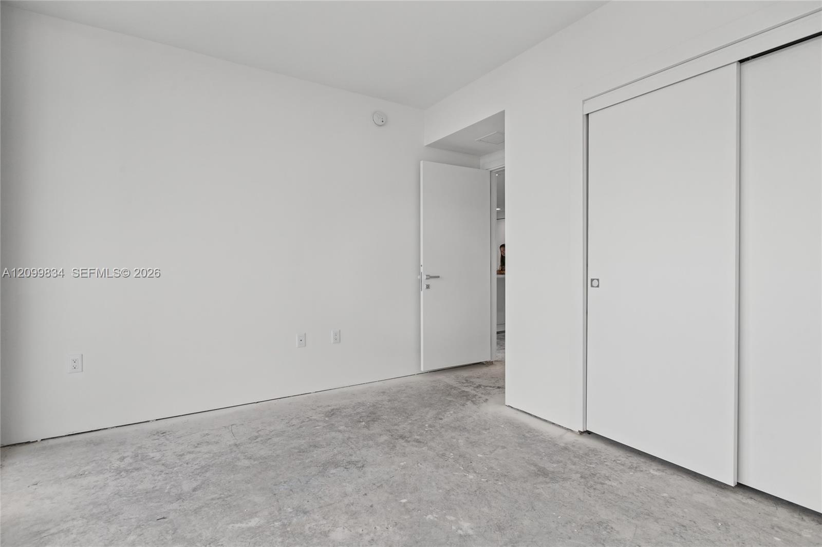 Minimalist interior featuring smooth white walls, sliding closet doors, a solid-core swing door, and concrete flooring