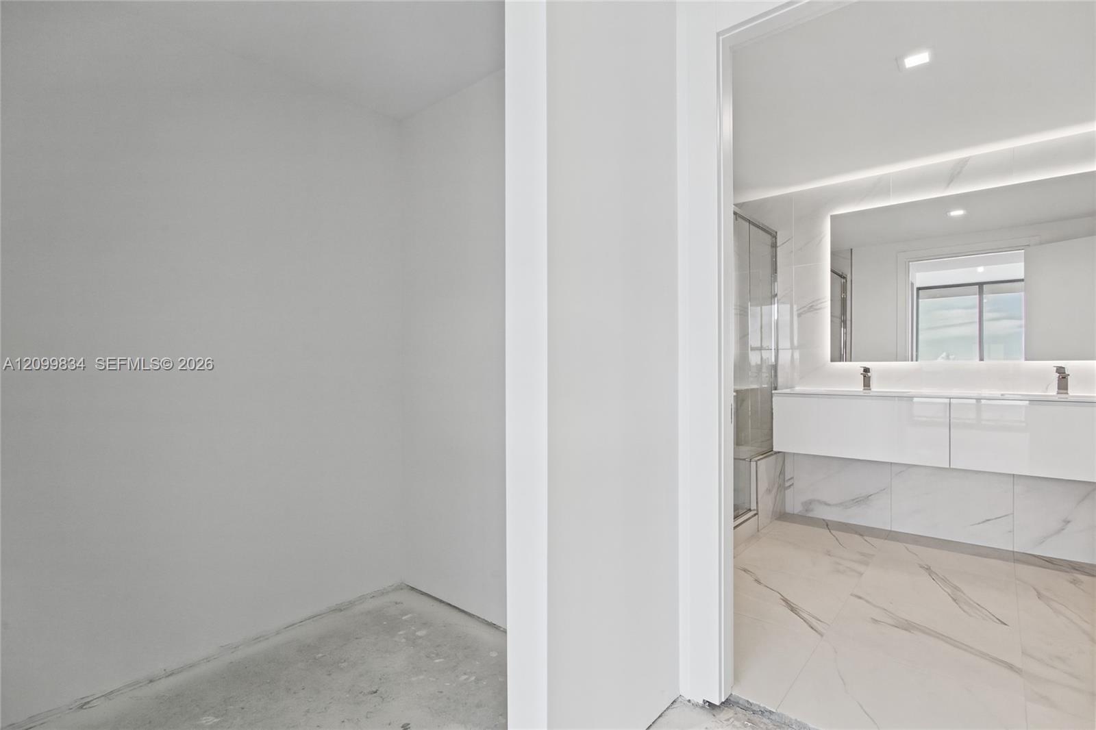 Bathroom featuring large-format tile flooring with stone-pattern detailing, white wall-mounted double vanity, integrated LED-backlit mirror, and glass