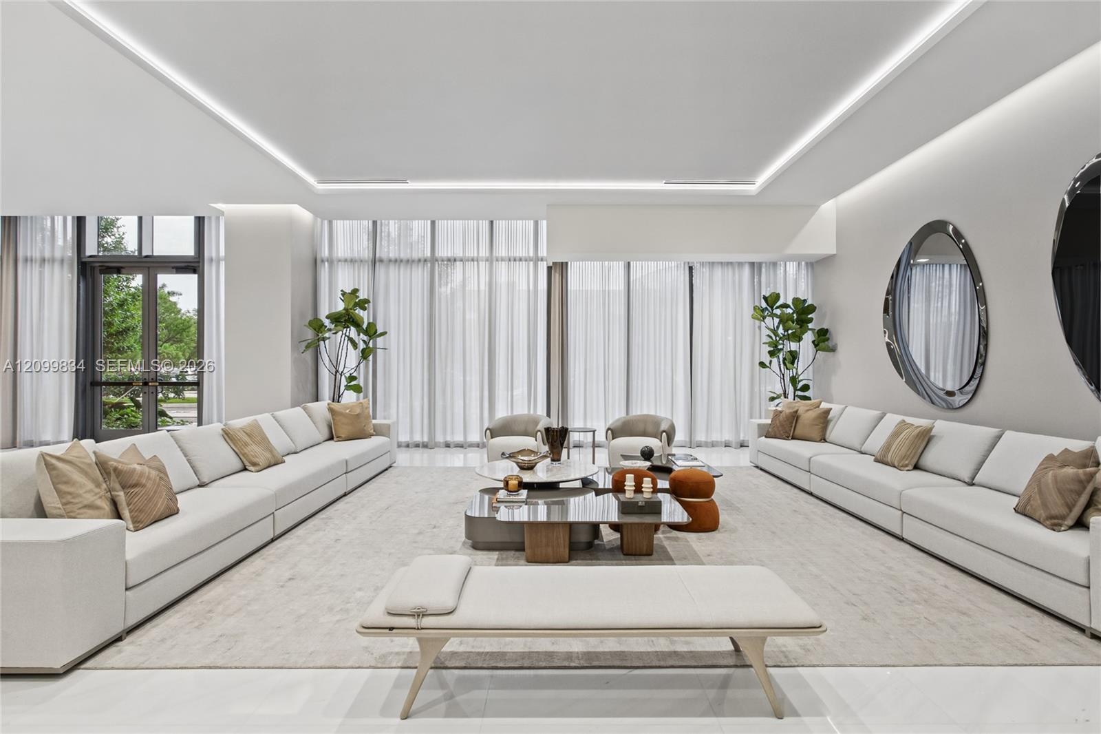 Expansive room featuring soaring ceilings with recessed cove lighting, floor-to-ceiling windows, and polished stone flooring