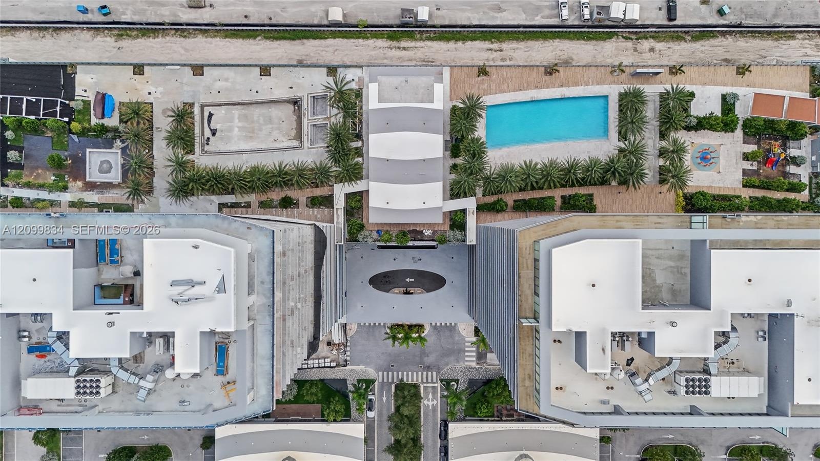 Aerial perspective featuring a central swimming pool, landscaped palm tree courtyards, paved pedestrian walkways, and structured surface parking