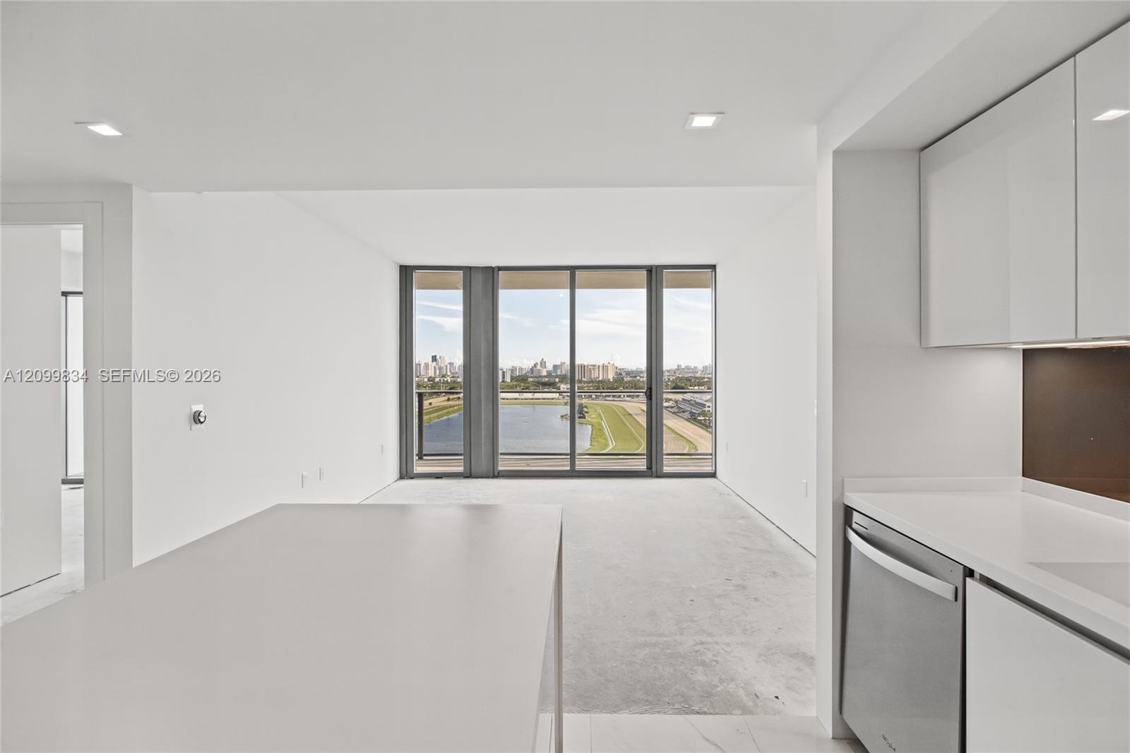 Kitchen featuring high-gloss white cabinetry, white stone countertops, built-in stainless steel dishwasher, recessed lighting, and floor-to-ceiling gl