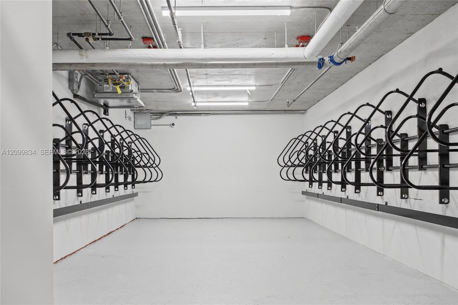 Dedicated storage room featuring wall-mounted metal bicycle racks, concrete flooring, and linear fluorescent lighting