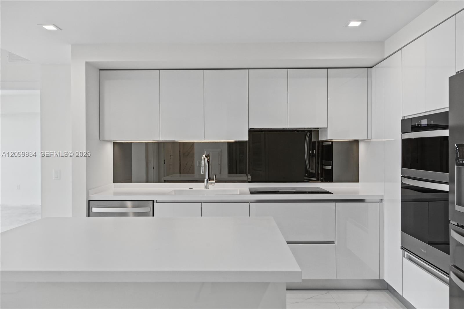 Kitchen featuring high-gloss white cabinetry, white stone countertops, a dark mirrored backsplash, integrated double wall ovens, and recessed lighting