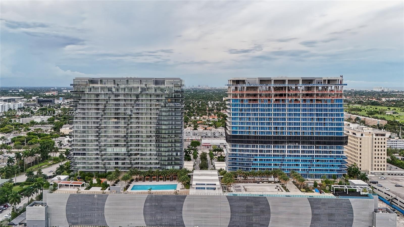 Aerial perspective of two high-rise towers featuring glass-paneled facades, integrated balconies, a ground-level swimming pool, and structured parking