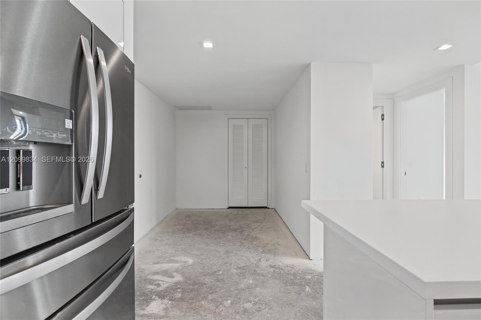 Stainless steel French-door refrigerator, crisp white cabinetry, quartz-style countertop, and double-panel louvered closet doors