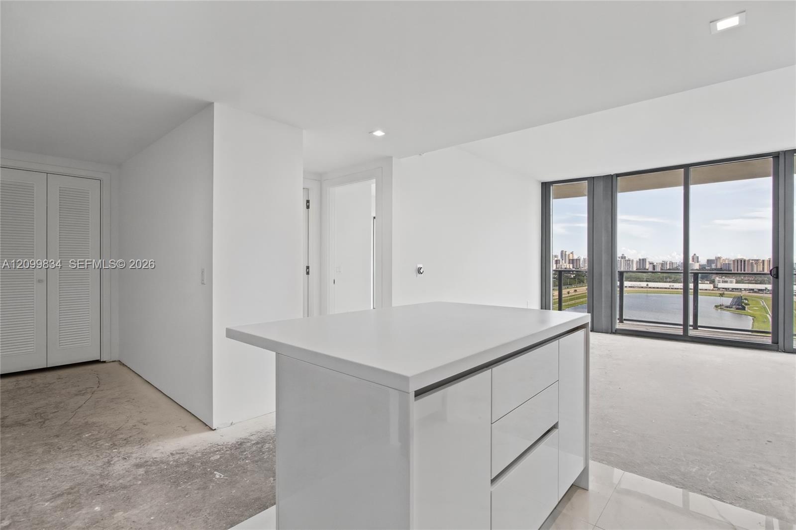 Kitchen island with a white countertop and flat-panel cabinetry, floor-to-ceiling glass sliding doors, and balcony with metal railing