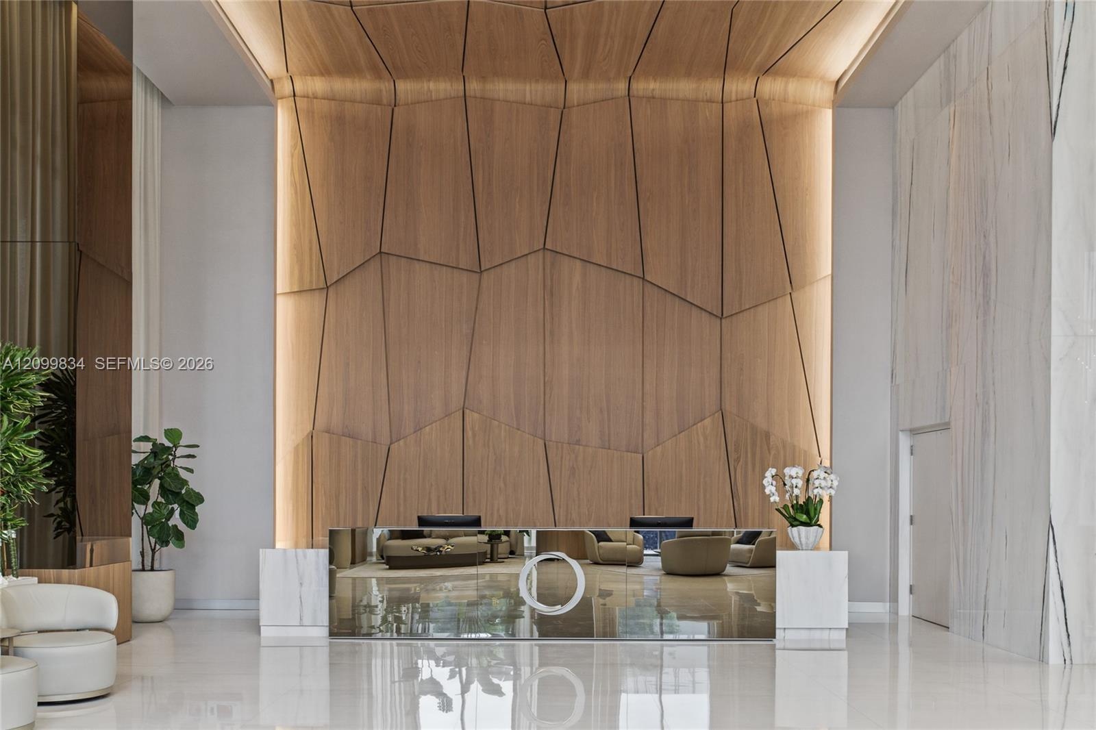 Double-height ceiling, geometric wood-paneled accent wall with integrated perimeter lighting, reflective mirrored reception desk, and large-format pol
