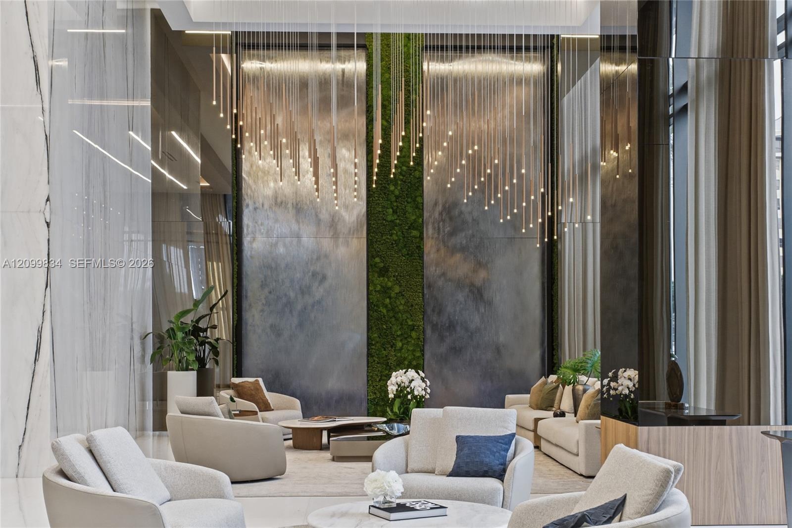 Double-height lobby featuring floor-to-ceiling stone wall panels, a vertical moss installation, metallic wall accents, and an extensive suspended pend