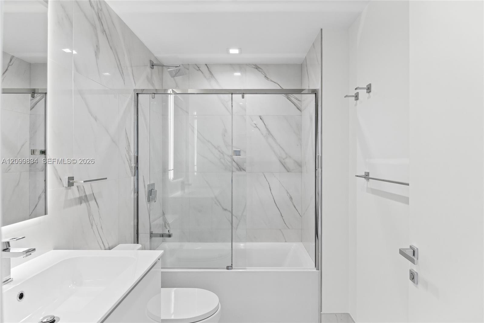 Bathroom featuring floor-to-ceiling stone-finish tile surround, a built-in bathtub with a chrome-framed sliding glass enclosure, a wall-mounted vanity