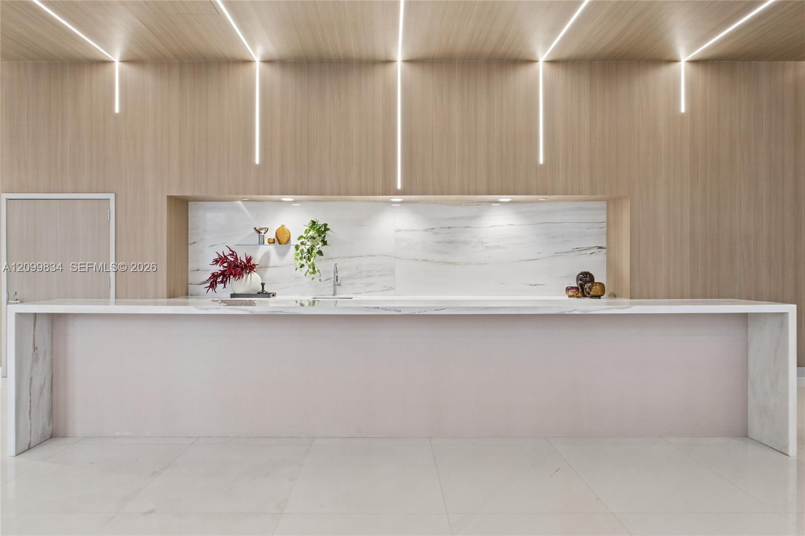 Custom kitchen island featuring a waterfall stone countertop, integrated vertical linear LED lighting, wood-paneled feature wall, and stone slab backs