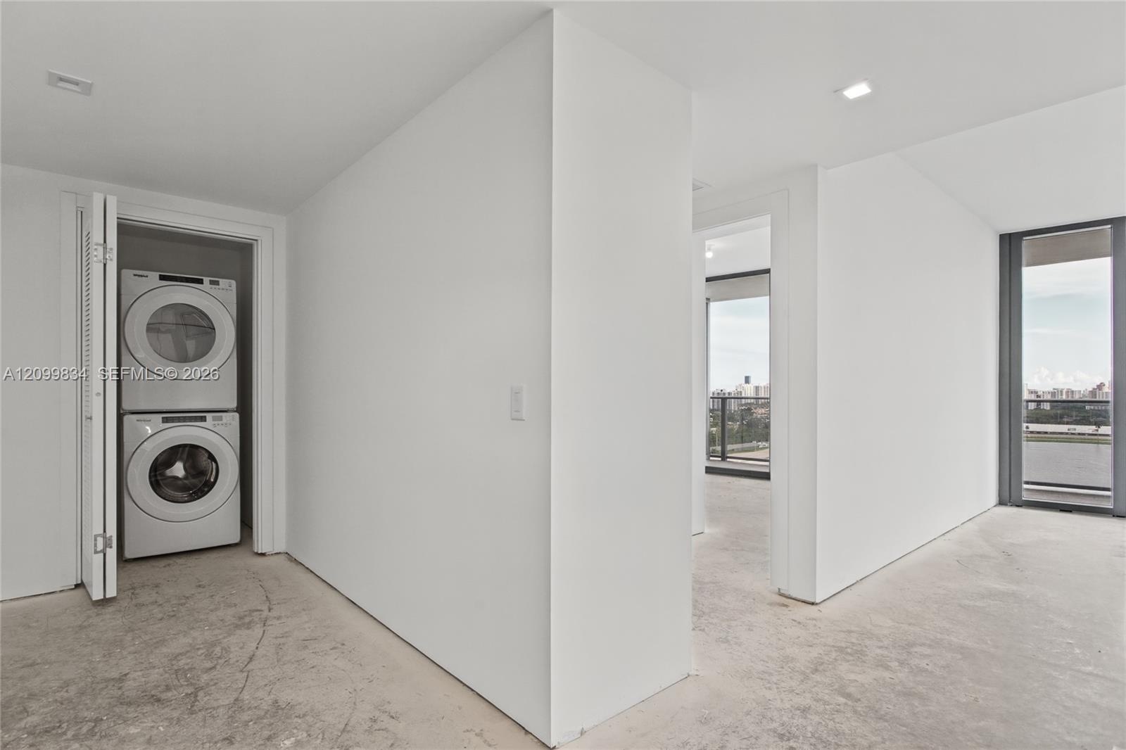 Stacked laundry unit enclosed in a louvered-door closet featuring white walls, recessed ceiling lighting, and floor-to-ceiling windows