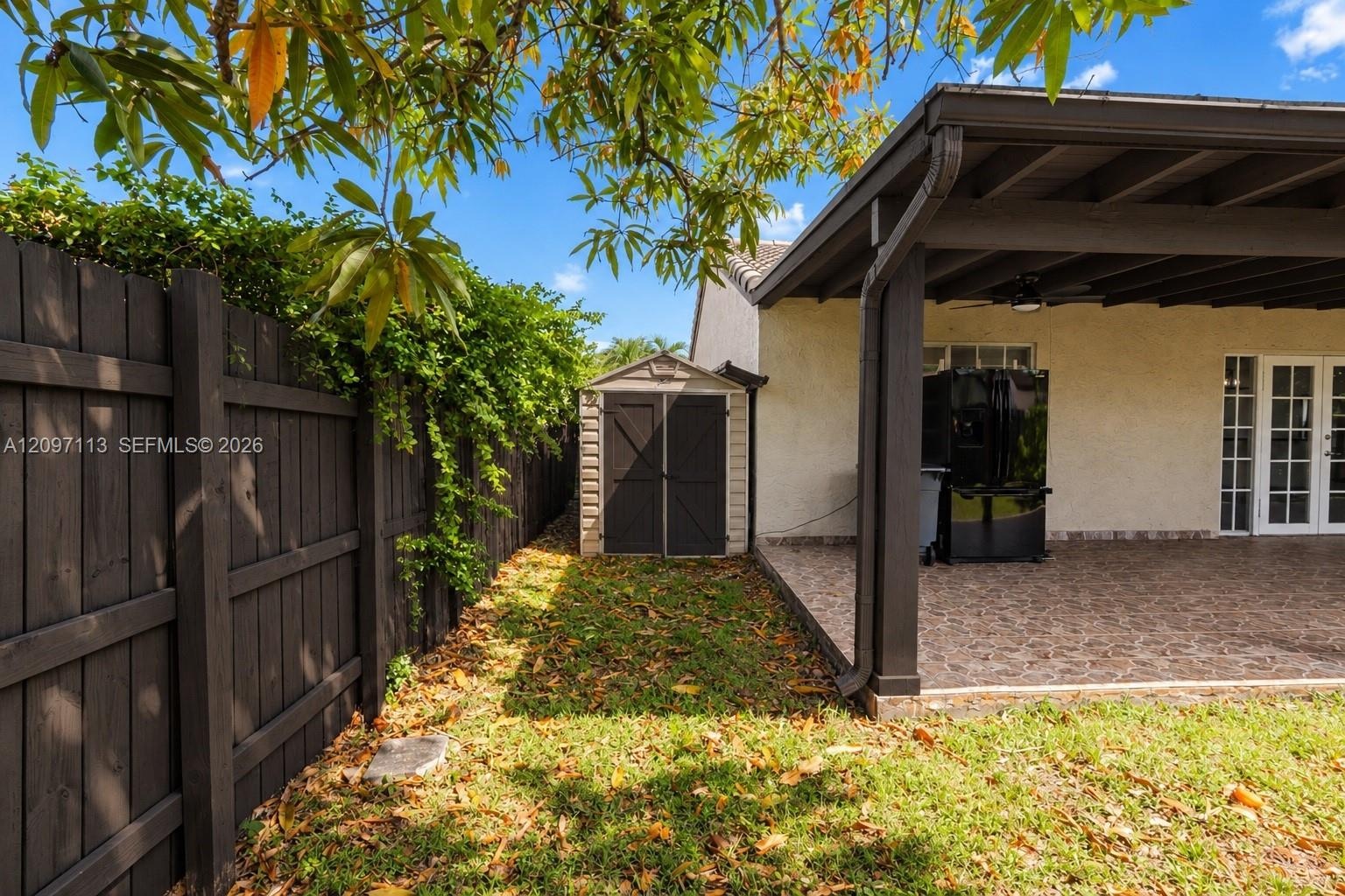Covered patio featuring patterned flooring, dark support columns, manicured lawn, and perimeter wood fencing