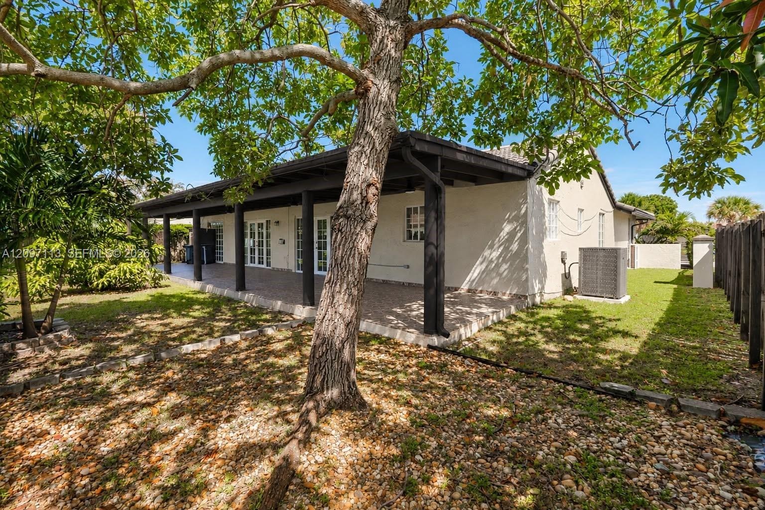 Stucco exterior side yard featuring a covered patio with tile flooring, enclosed by a dark wood privacy fence