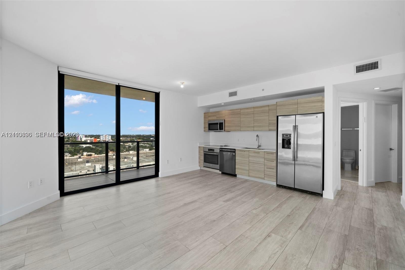 Open-concept living space featuring wood-finish flooring, floor-to-ceiling glass sliding doors, horizontal wood-grain cabinetry, stainless steel appli