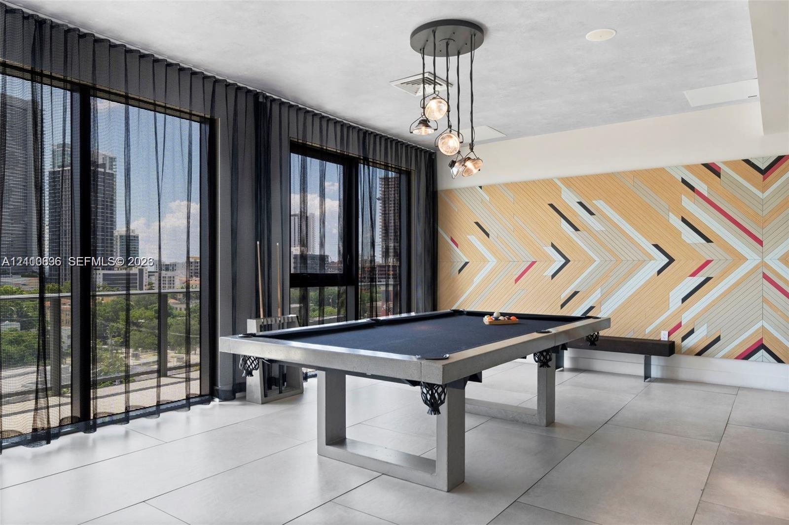 Modern recreation room featuring a regulation pool table, geometric wood-finish accent wall with multi-colored chevron detailing, floor-to-ceiling gla