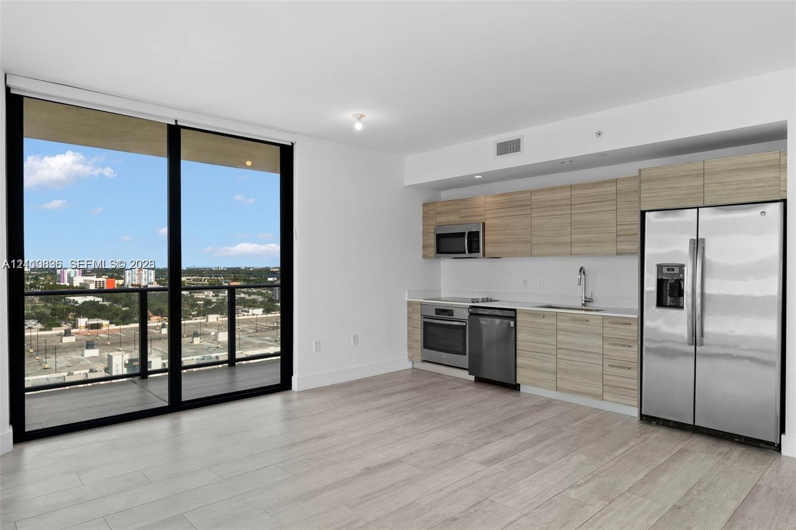 Kitchen featuring wood-finish cabinetry, stainless steel appliances, and quartz countertops, complemented by wood-finish flooring and floor-to-ceiling
