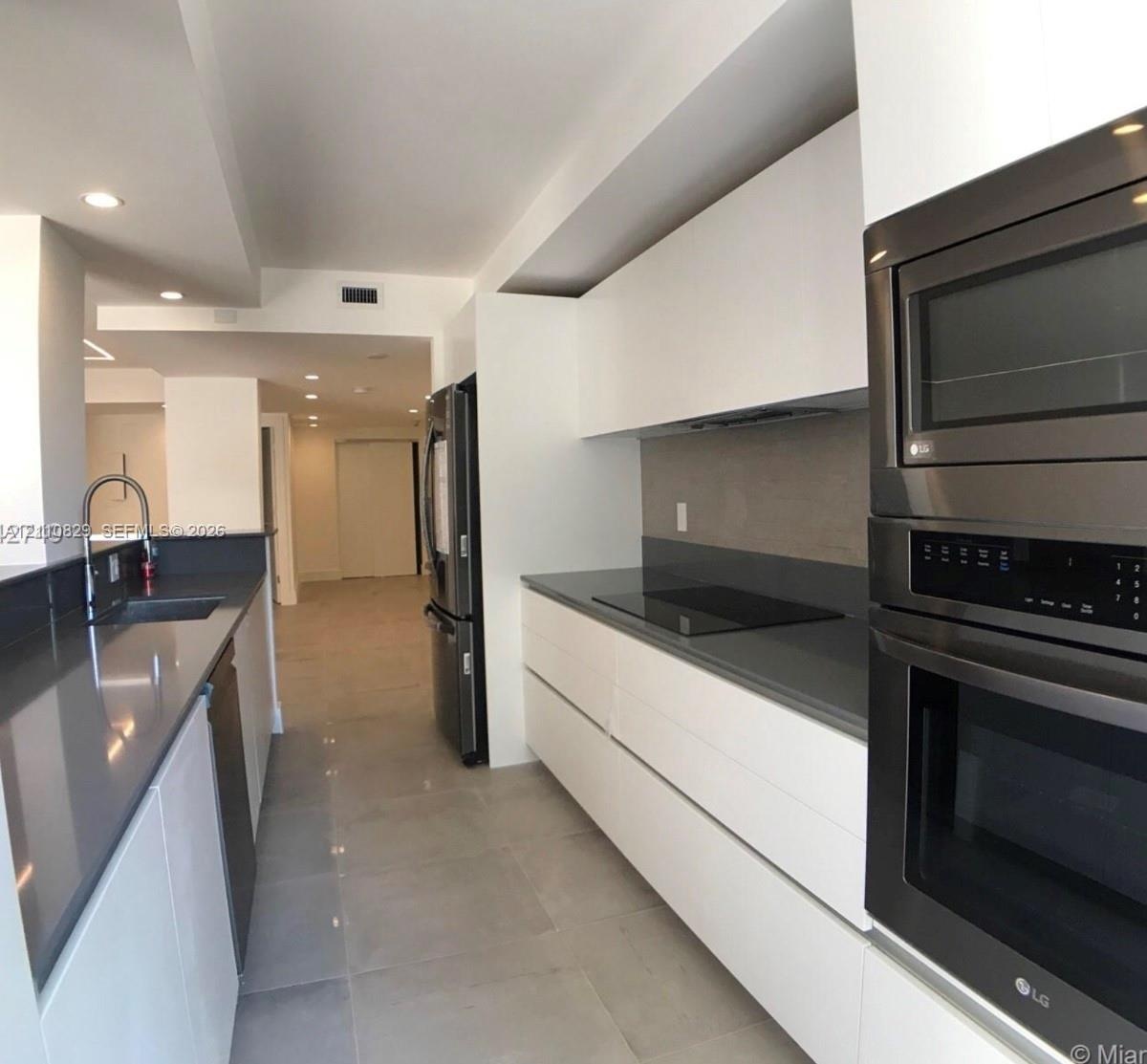 Sleek kitchen featuring flat-panel white cabinetry, quartz countertops, a smooth-surface cooktop, stainless steel wall-mounted oven and microwave, and