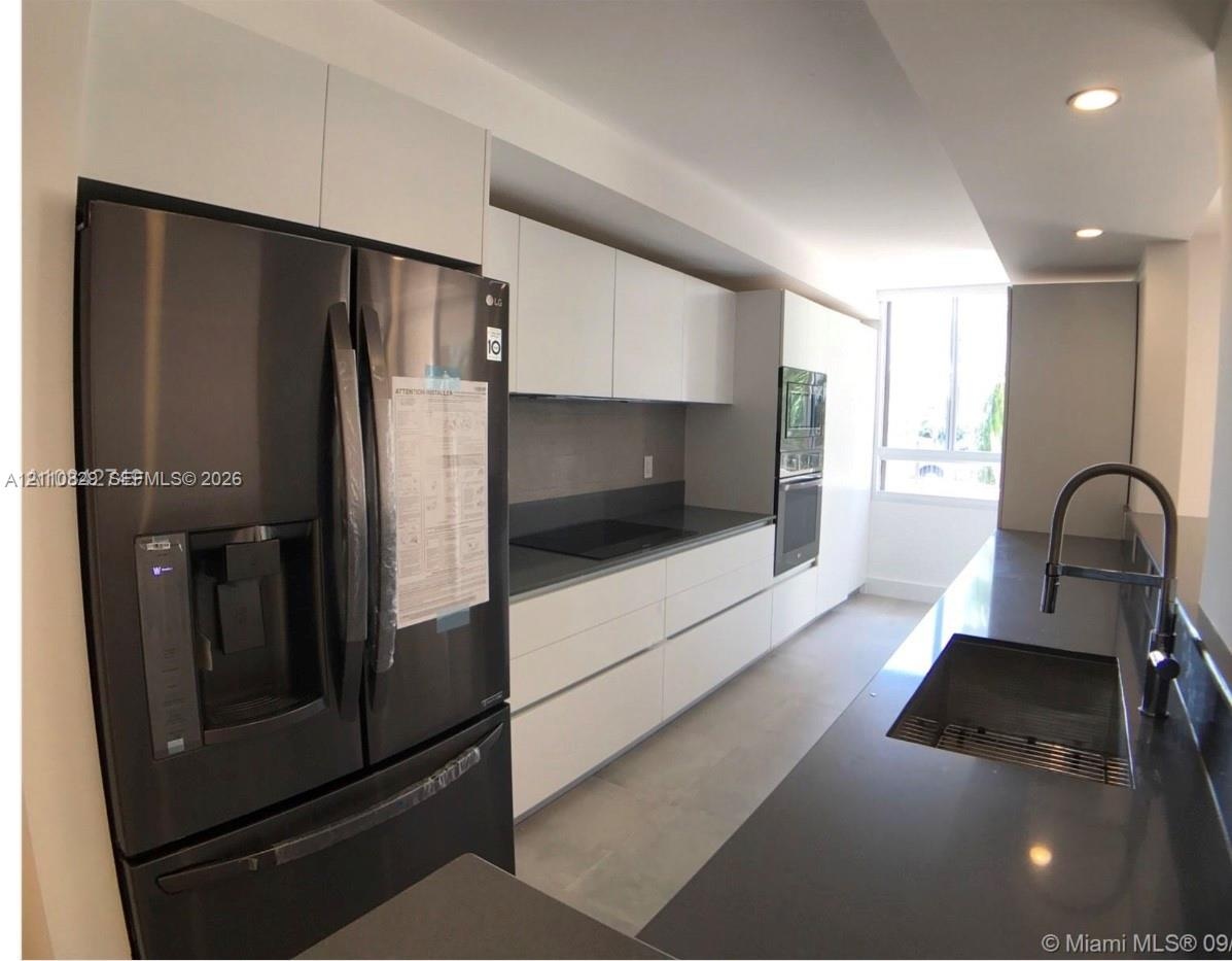 Modern kitchen featuring high-gloss white flat-panel cabinetry, dark solid-surface countertops, built-in stainless steel oven, integrated cooktop, and