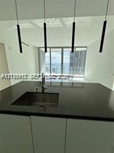 Modern kitchen island featuring a solid-surface countertop, integrated stainless steel undermount sink, gooseneck faucet, and four cylindrical pendant