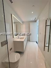 Modern bathroom featuring floor-to-ceiling tile, a floating dual-sink vanity with integrated lighting, a wall-mounted toilet, and a glass-enclosed sho