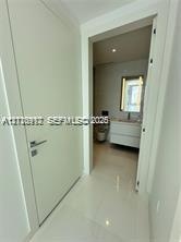Solid-core white interior door with a contemporary metallic handle, polished tile flooring, wall-mounted floating vanity with integrated basin, and il