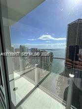 Private balcony featuring glass railings and tile flooring, overlooking urban skyline and coastal water