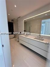 Floating dual-sink vanity with matte finishes, quartz countertop, large backlit mirror, and freestanding soaking tub