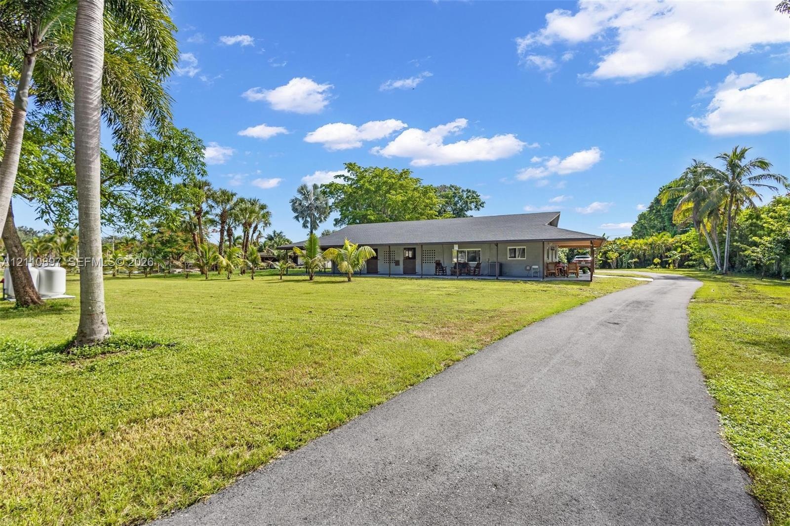 Single-story residence featuring a covered front porch, asphalt driveway, and expansive lawn with mature palm trees