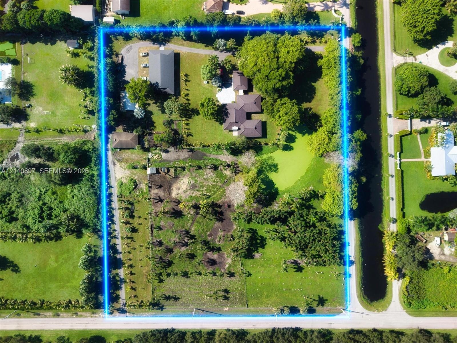 Expansive acreage featuring a multi-structure footprint, mature tree canopy, integrated canal frontage, and a private paved driveway