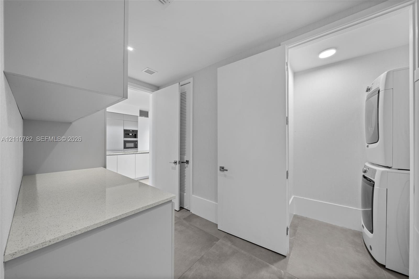 Utility area featuring stone-surface countertop, built-in cabinetry, large-format tile flooring, and dedicated laundry closet with stacked appliance c