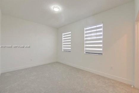 Neutral-toned carpeted flooring, white wall finishes, dual windows featuring adjustable banded roller shades, and a central flush-mount ceiling light 