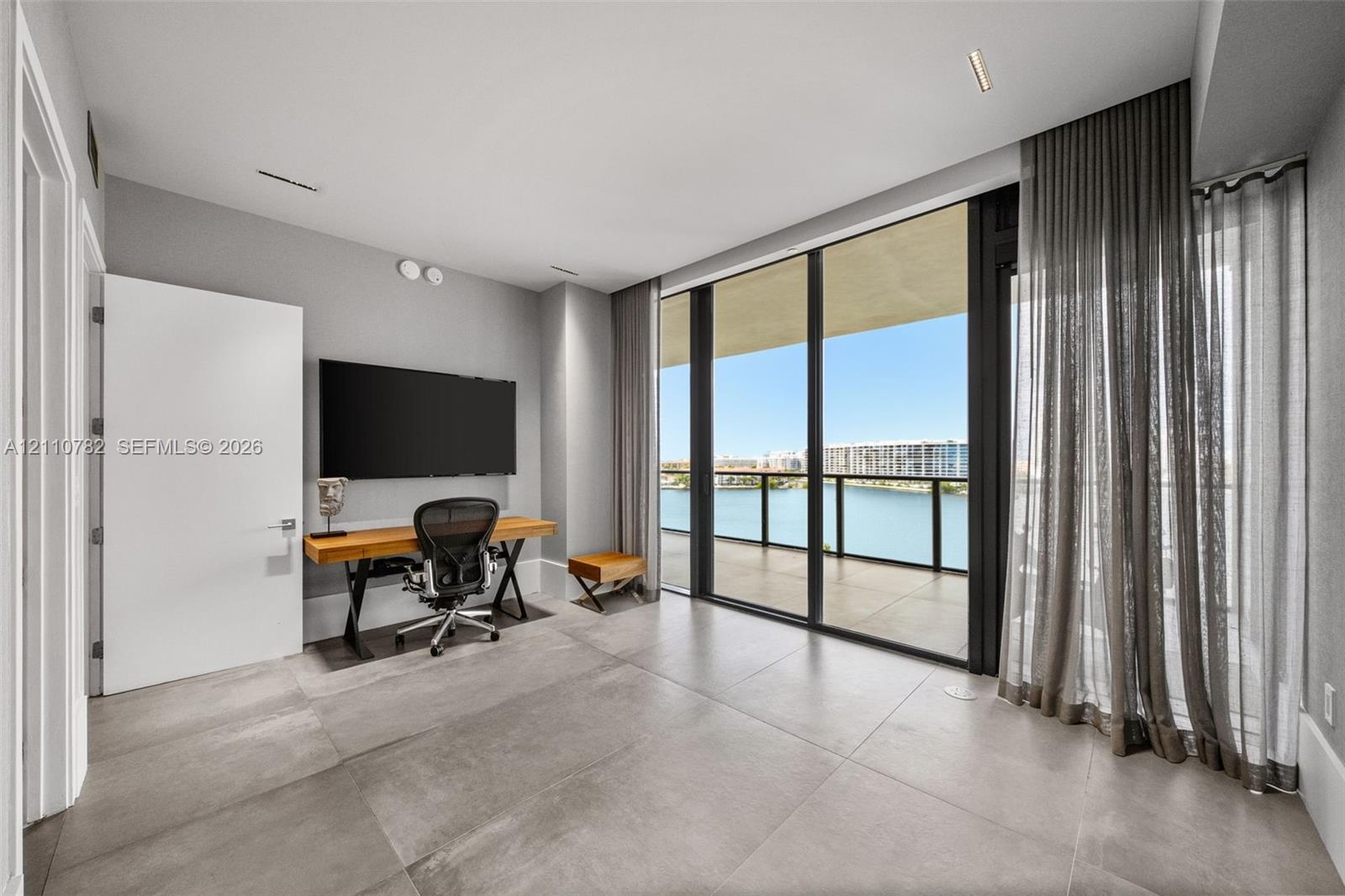 Floor-to-ceiling glass wall, large-format tile flooring, recessed ceiling lighting, and covered balcony featuring a glass panel railing