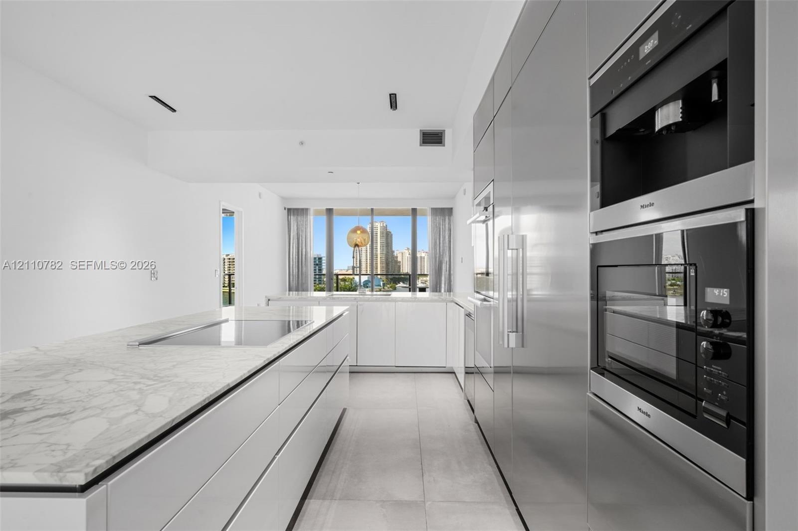 Contemporary kitchen featuring a stone-surface island with an integrated cooktop, flat-panel cabinetry, high-end built-in stainless steel appliances, 