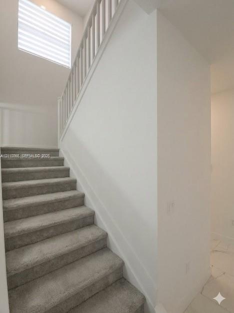 Staircase featuring neutral carpeting, white vertical balusters, and a high-reaching window with integrated blinds