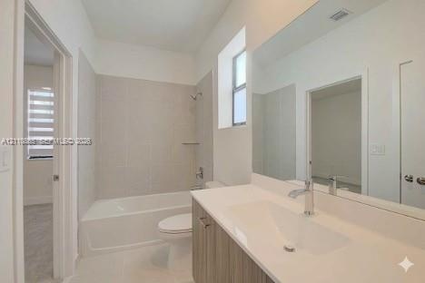 Bathroom featuring a wood-finish vanity with a white integrated sink, full-width wall mirror, and a tub-shower combination with floor-to-ceiling tile 