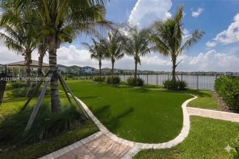 Backyard featuring artificial turf, paver walkways, mature palm trees, a perimeter metal fence, and water frontage
