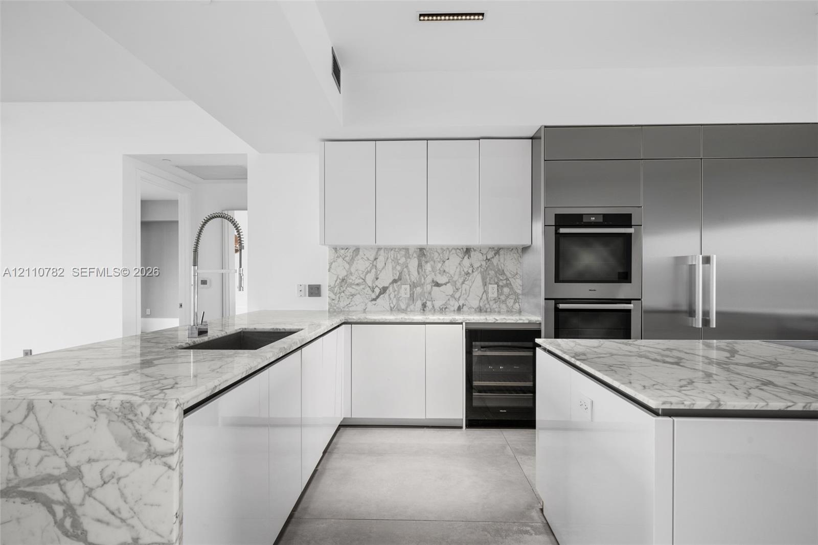 Kitchen featuring white flat-panel cabinetry, stone countertops with waterfall edge, full-height stone backsplash, stainless steel double wall ovens, 