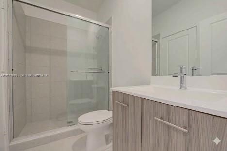 Bathroom featuring a vanity with a light wood-finish cabinet and an integrated countertop, a glass-enclosed shower with tiled surround, and a wall-mou