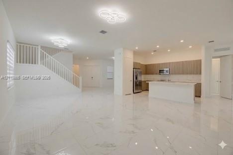 Open-concept interior featuring large-format polished stone flooring, custom wood-finish cabinetry, a central kitchen island, recessed ceiling lightin