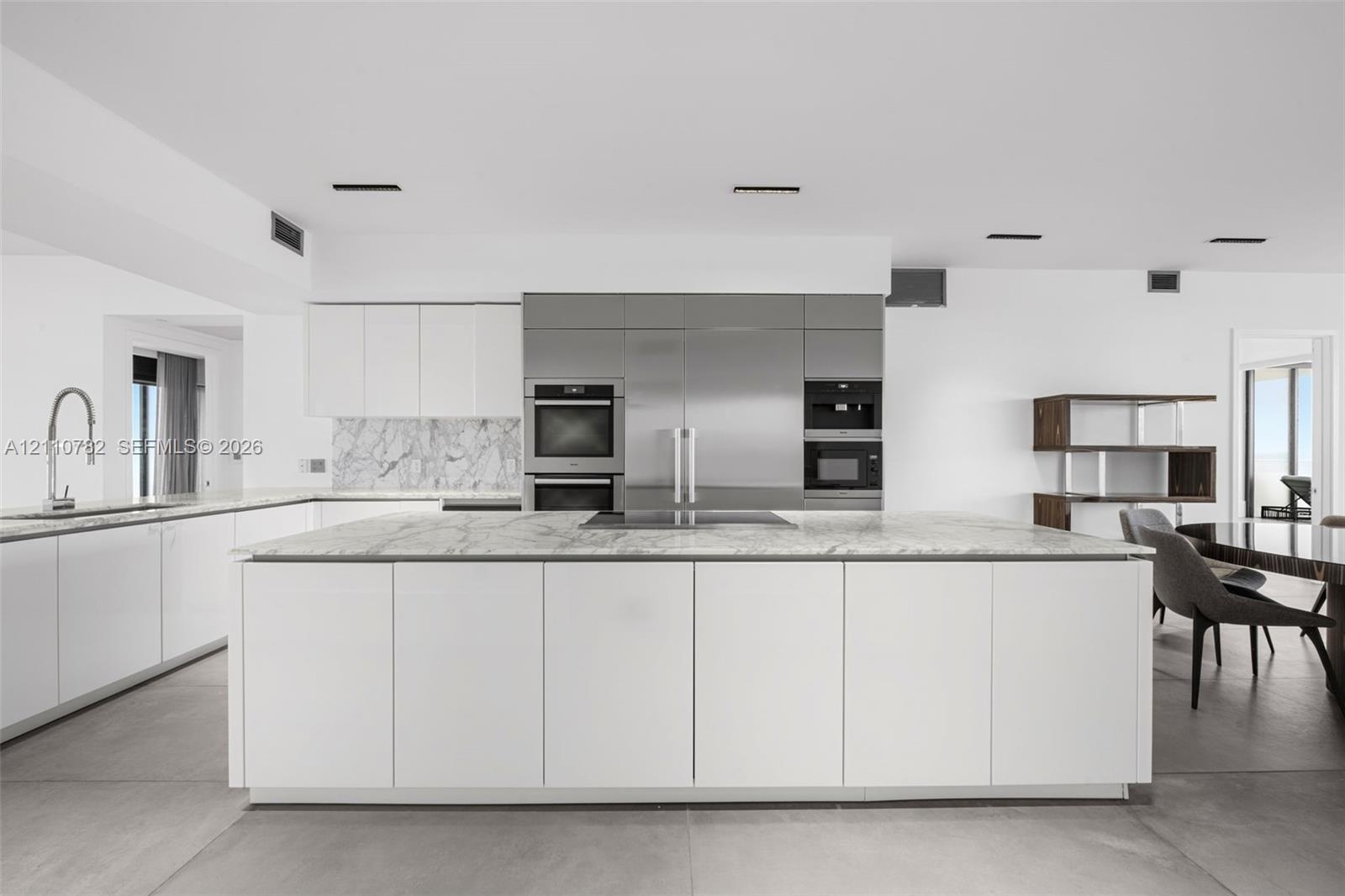 Contemporary kitchen featuring an expansive center island with stone surfacing, stainless steel built-in appliances, flat-panel cabinetry, a stone bac