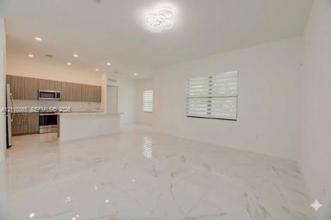 Open-concept interior featuring large-format stone-finish tile flooring, horizontal-slat window shades, recessed lighting, and a modern kitchen with f