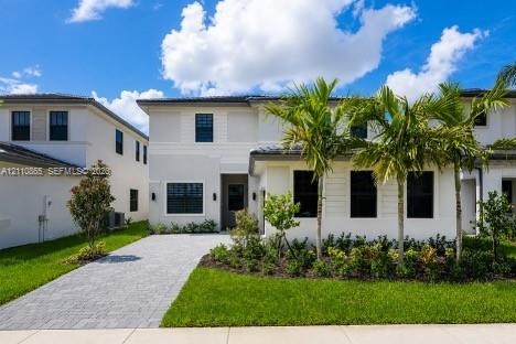 Two-story exterior featuring light-toned smooth stucco finish, horizontal siding accents, dark-framed windows, paver driveway, and professional landsc
