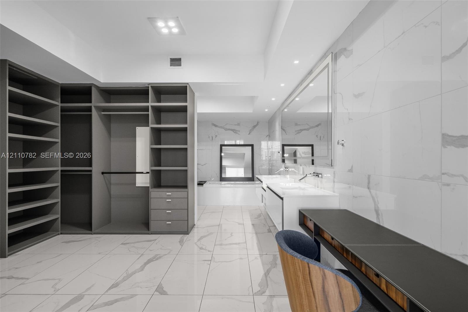 Custom built-in storage system with grey cabinetry, large-format tiled flooring, wall-to-wall vanity with dual sinks, and full-height tiled wall detai
